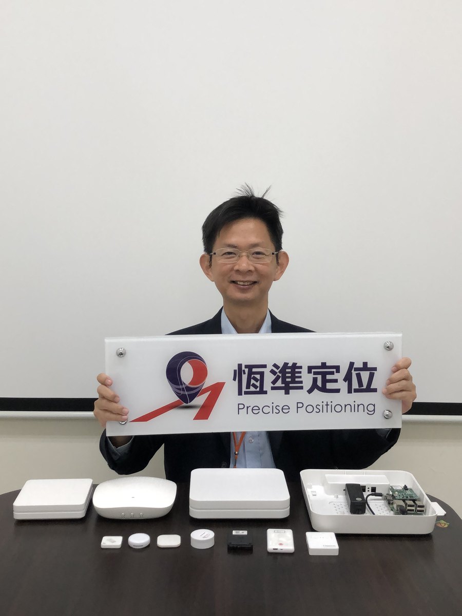 Dr. Jeremy Kuo, founder and CEO of P-Square, holding the Precise Positioning brand sign, with the company's own UWB anchors, Bluetooth locators, tags and gateways on the desk